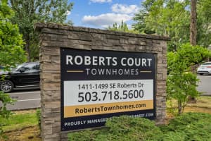 Stone-framed townhome community sign surrounded by shrubs and mature trees at Roberts Court Townhomes in Gresham, Oregon