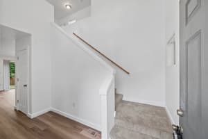 Carpeted staircase with wood handrail and white half-wall beside entry at Roberts Court Townhomes in Gresham, Oregon
