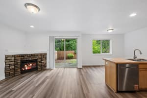 Open living room with stone fireplace, wood-look flooring, and sliding glass door at Roberts Court Townhomes in Gresham, Oregon