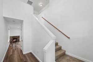 Carpeted stairs with a wood handrail beside a wood-look hallway at Roberts Court Townhomes in Gresham, Oregon