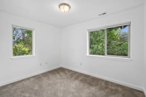 Carpeted bedroom with two windows overlooking leafy trees at Roberts Court Townhomes in Gresham, Oregon