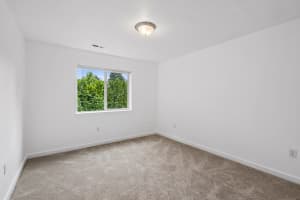 Carpeted bedroom with white walls and a window overlooking greenery at Roberts Court Townhomes in Gresham, Oregon