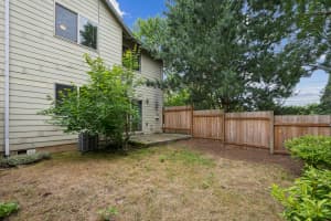 Concrete patio beside a wood-fenced yard with mature trees at Roberts Court Townhomes in Gresham, Oregon