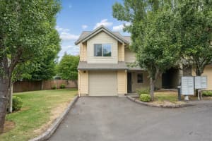 Two-story townhome with attached garage, beige siding, and mature trees at Roberts Court Townhomes in Gresham, Oregon
