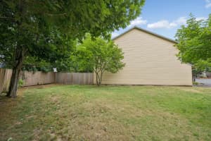 Townhome side exterior with a grassy lawn, mature trees, and wood fence at Roberts Court Townhomes in Gresham, Oregon