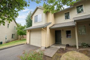 Two-story townhome with attached garage, covered entry, and beige siding at Roberts Court Townhomes in Gresham, Oregon