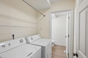 Laundry area with white washer, dryer, wire shelf, and hanging rod at Roberts Court Townhomes in Gresham, Oregon