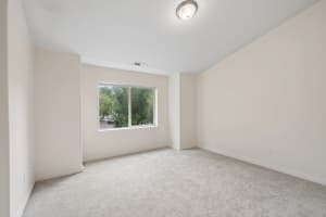 Carpeted bedroom with a large window overlooking leafy trees at Roberts Court Townhomes in Gresham, Oregon