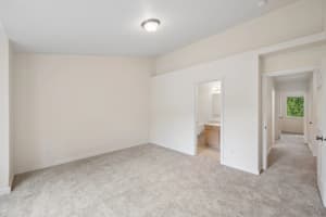 Carpeted bedroom with an attached bathroom and open hallway doorway at Roberts Court Townhomes in Gresham, Oregon