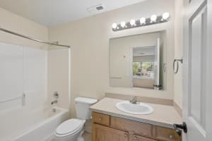 Bathroom with wood vanity, large mirror, globe lighting, and white bathtub at Roberts Court Townhomes in Gresham, Oregon