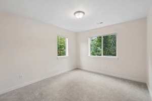 Carpeted bedroom with two windows overlooking leafy trees at Roberts Court Townhomes in Gresham, Oregon