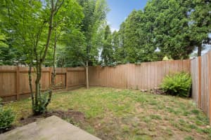 Fenced backyard with mature trees, grass, and a concrete patio at Roberts Court Townhomes in Gresham, Oregon