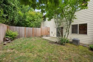 Concrete patio beside a fenced grassy yard with mature trees at Roberts Court Townhomes in Gresham, Oregon